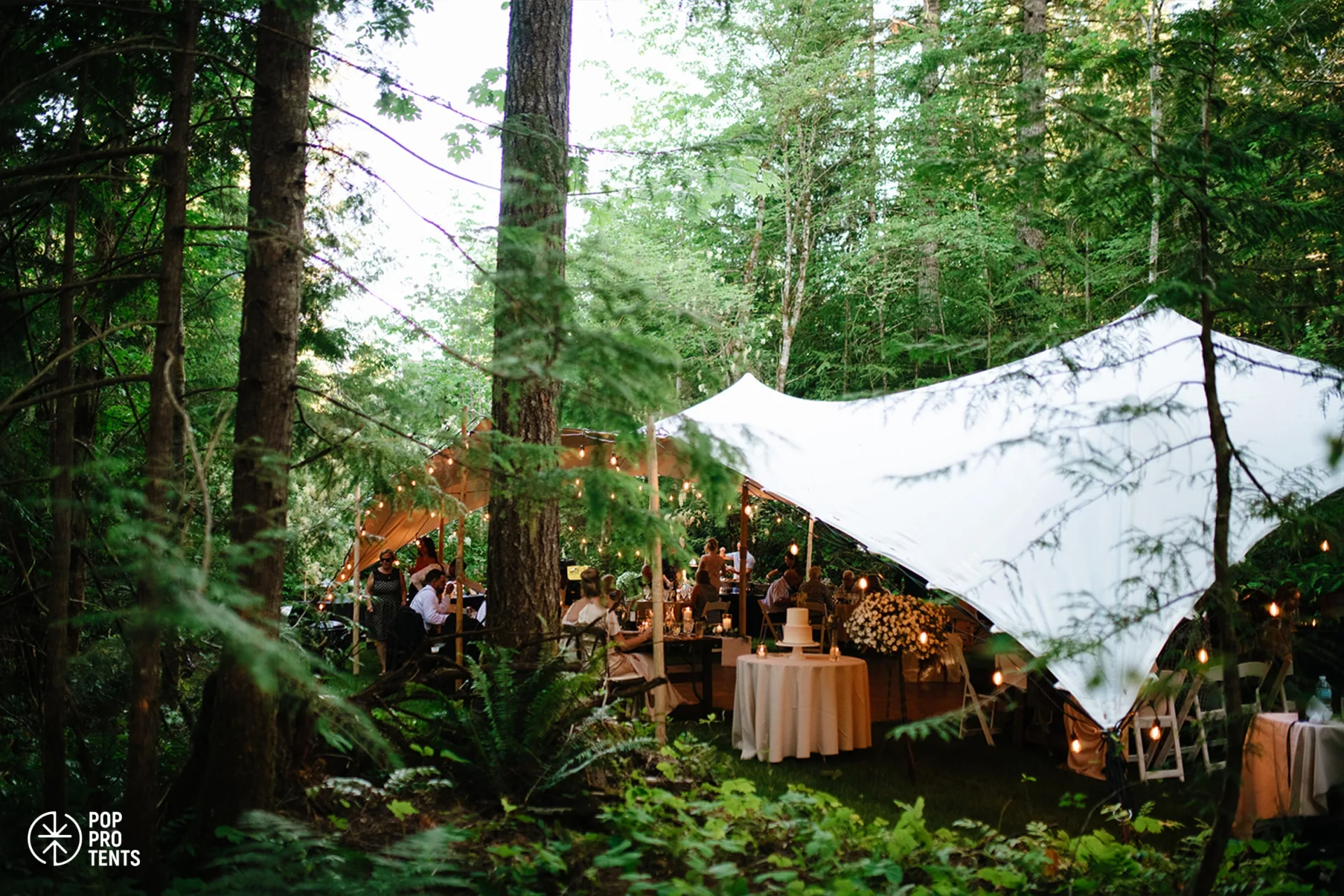 Evening wedding feast under stretch tent in woodland setting